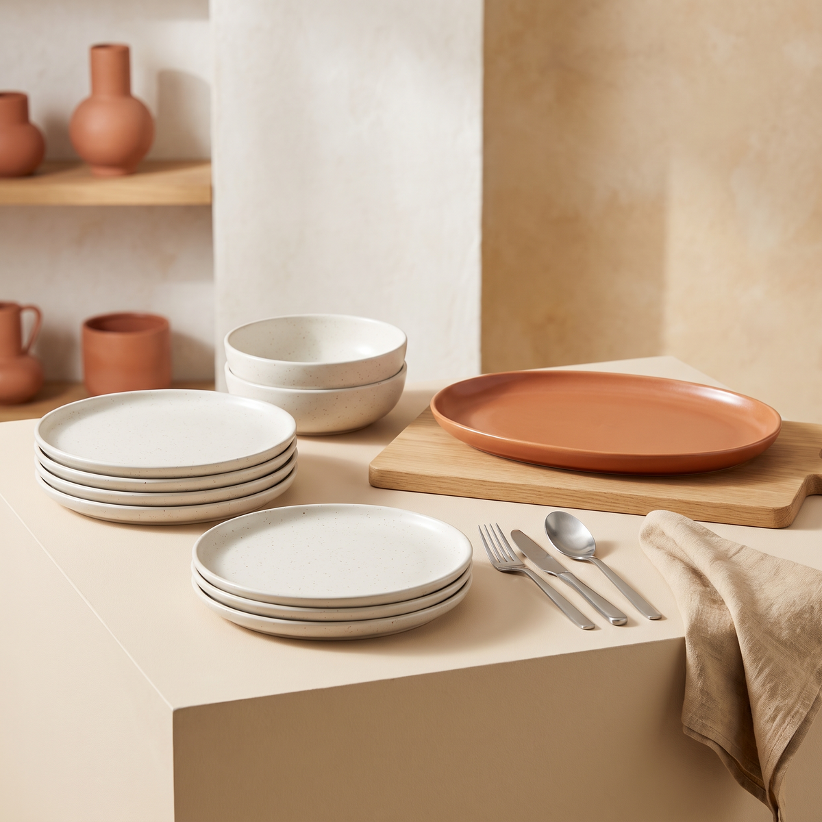 Speckled ceramic plates and bowls with a terracotta platter, oak board and cutlery