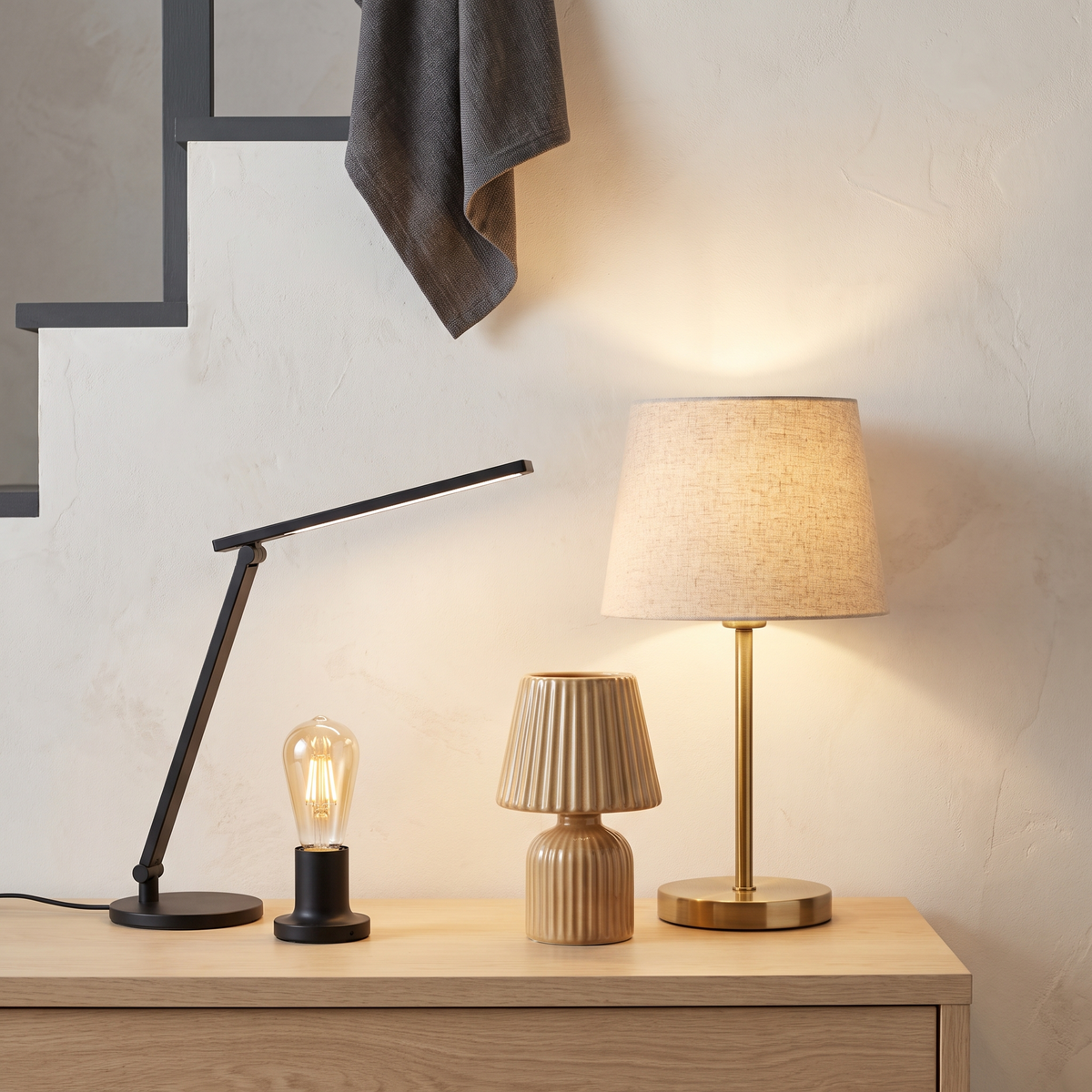 Brass table lamp, ceramic bedside lamp, LED desk lamp and smart bulb lit against a wall