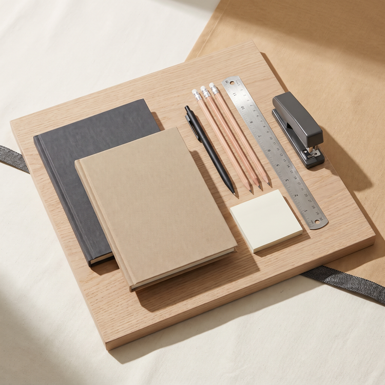 Linen-bound notebooks with a matte black pen, pencils, ruler and stapler