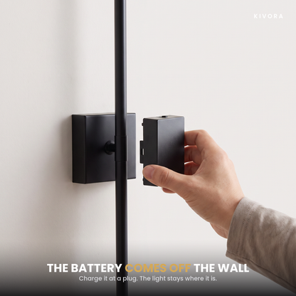 A hand sliding the battery box off the wall plate — charge it at a plug while the light stays on the wall
