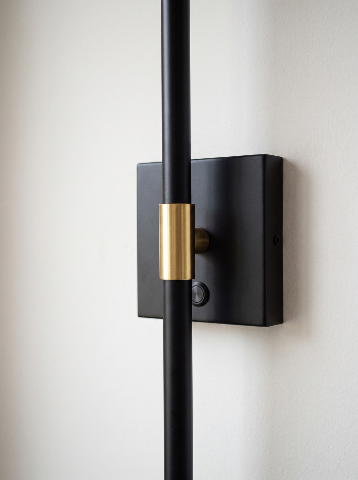 Close view of the square wall plate with the bar crossing it and a brass collar at the join, with a touch button on the plate and no cable on the wall