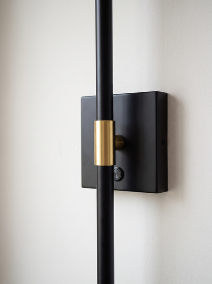 Close view of the square wall plate with the bar crossing it and a brass collar at the join, with a touch button on the plate and no cable on the wall